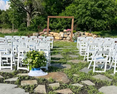 A wooden ceremony arbor with white chairs on the lawn