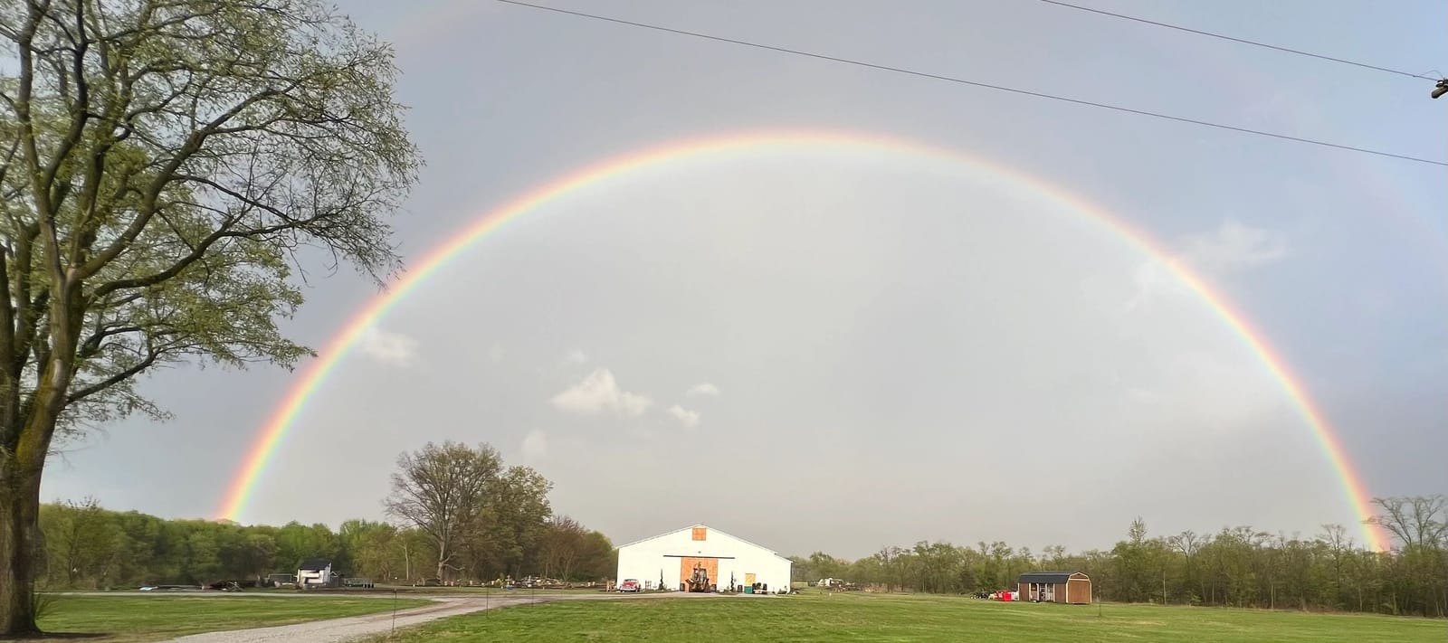 A full rainbow arching over the white DnB Barn in Knox, Indiana