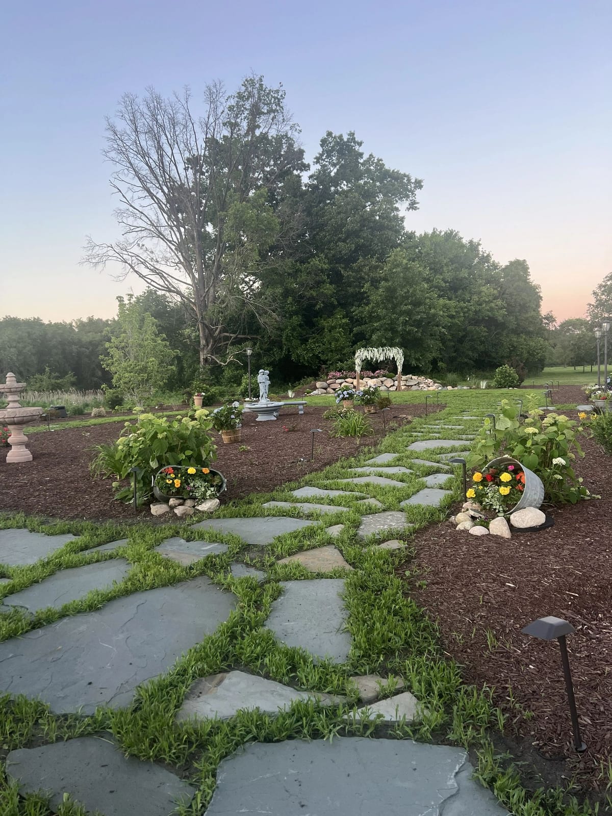 The DnB Barn flower garden at golden hour, with stone pathways, a rock wall, and the pondless waterfall